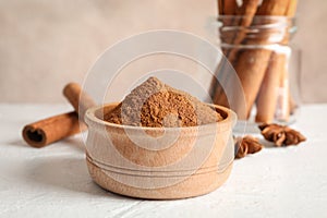 Bowl with cinnamon powder, cinnamon sticks and anise on white background