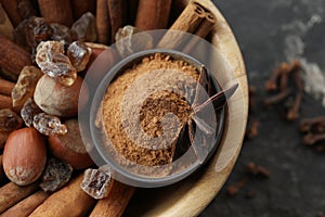 Bowl with cinnamon sticks, powder, sugar and hazelnuts on table, closeup