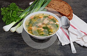 Bowl of clear salmon soup, greens, bread, spoon on napkin