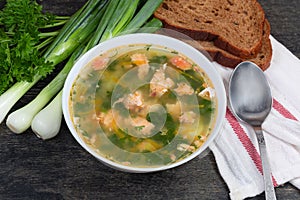 Bowl of clear salmon soup, greens, bread, spoon on napkin