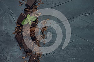 Bowl with cocoa powder, pieces of chocolate, chocolate shavings and mint on grey textured background. Top view. Flat lay. Copy