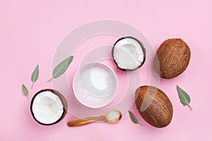 Bowl with coconut oil and fresh half of coconuts on pink table top view. Beauty and spa homemade cosmetic. Flat lay.