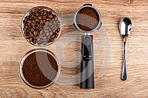 Bowl with coffee beans, holder from coffeemaker with ground coffee, bowl with ground coffee, spoon on table. Top view