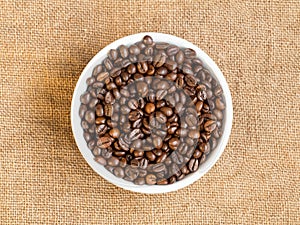 Bowl with coffee beans, on sackcloth background, flat lay