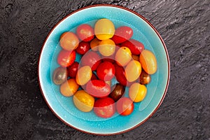 Bowl of colorful cherry tomatoes red, garnet and yellow, fresh and raw. With water drops. On black textured background and space