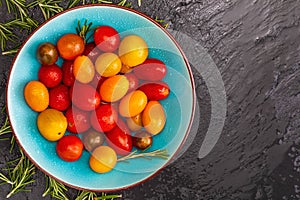 Bowl of colorful cherry tomatoes red, garnet and yellow, fresh and raw. With water drops and rosemary. On black textured