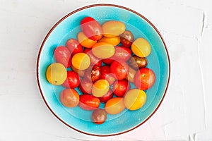 Bowl of colorful cherry tomatoes red, garnet and yellow, fresh and raw. With water drops On white textured background and space