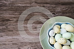 Bowl with colorful Easter eggs on blue plate, wooden background