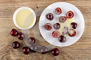 Bowl with condensed milk, cherries with condensed milk in saucer, cherry on table. Top view