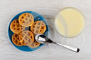 Bowl with condensed milk, soft waffles in blue saucer, spoon on table. Top view