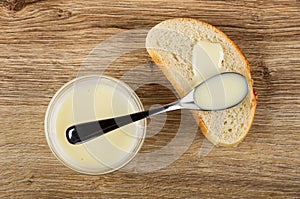 Bowl with condensed milk, spoon on slice of bread on wooden table. Top view