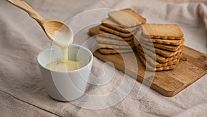 Bowl with condensed milk with wooden spoon and biscuits in the background