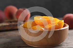 Bowl with conserved peach halves on wooden table