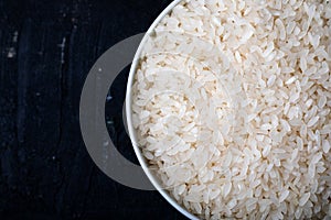 Bowl containing uncooked white rice on a black background. Top view. Close-up. Background and texture.