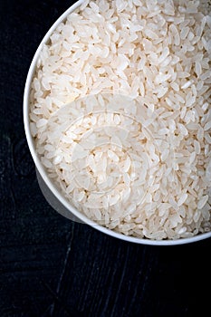Bowl containing uncooked white rice on a black background. Top view. Close-up. Background and texture.