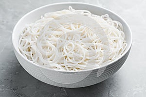 Bowl with cooked rice noodles on light marble table, closeup