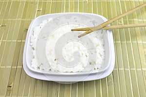 A bowl of cooked white rice with chopsticks on bamboo background