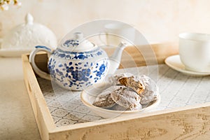 Bowl with cookies, white tea cups, tea pot on a tray set for breakfast