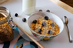 Bowl of corn flakes with blackberries next to the milk and corn flake jars