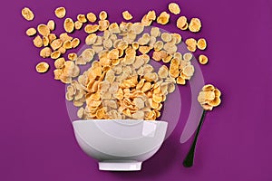 Bowl with corn flakes and spoon on purple background, top view