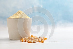 Bowl with corn flour and kernels on table against color background.