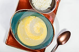Bowl of corn porridge with butter and cheese on white paper background close up.
