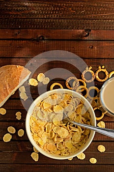 The bowl of cornflakes with glass of coffee drink and the piece of white bread on wooden background.