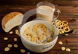 The bowl of cornflakes with glass of coffee drink and the piece of white bread on wooden background.