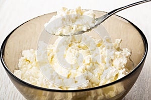 Bowl of cottage cheese with condensed milk, spoon with cottage cheese above bowl