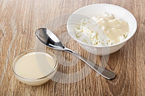 Bowl with cottage cheese and condensed milk, spoon, bowl with condensed milk on table