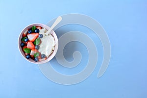 Bowl with cottage cheese, cream, strawberry, blueberry and mint leaves on blue background. Top view