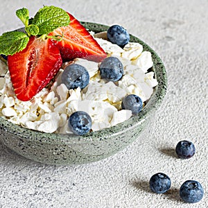 A bowl with cottage cheese, yogurt, fresh berries blueberries, strawberries and fresh mint on a gray background.