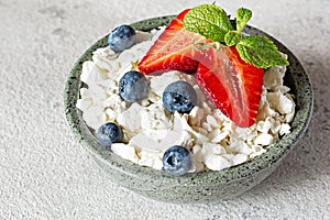 A bowl with cottage cheese, yogurt, fresh berries blueberries, strawberries and fresh mint on a gray background.