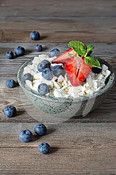 A bowl with cottage cheese, yogurt, fresh berries blueberries, strawberries and fresh mint on a wooden background.