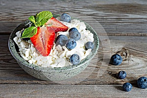 A bowl with cottage cheese, yogurt, fresh berries blueberries, strawberries and fresh mint on a wooden background.