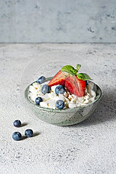 A bowl with cottage cheese, yogurt, fresh berries blueberries, strawberries and fresh mint on a gray background.