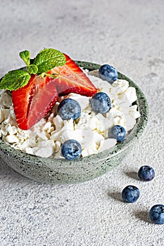 A bowl with cottage cheese, yogurt, fresh berries blueberries, strawberries and fresh mint on a gray background.