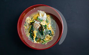 A bowl of creamy noodle soup with scramble eggs and leafy vegetables toppings on bblack baground