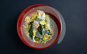 A bowl of creamy noodle soup with scramble eggs and leafy vegetables toppings on bblack baground photo