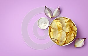 Bowl of crispy potato chips or crisps with sour cream and onion flavor on light purple background