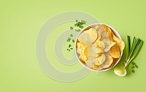 Bowl of crispy potato chips or crisps with spring onion flavor on light green background