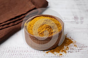 Bowl with curry powder on white wooden table, closeup