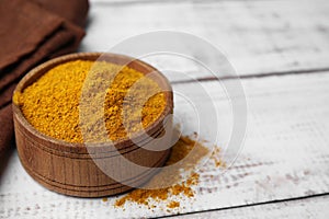 Bowl with curry powder on white wooden table, closeup. Space for text