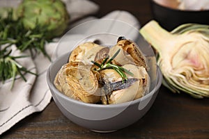 Bowl with delicious artichokes pickled in olive oil on wooden table, closeup