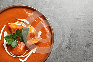 Bowl of delicious butter chicken on grey background, top view with space for text.