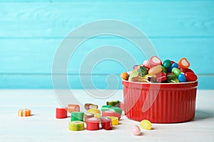 Bowl with delicious colorful candies on table against wooden background.