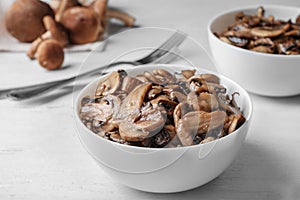 Bowl with delicious cooked mushrooms on white table