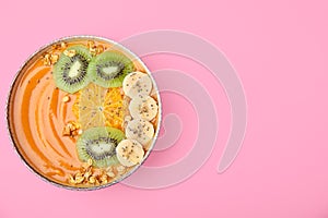 Bowl of delicious fruit smoothie with fresh banana, kiwi slices and granola on pink background, top view. Space for text
