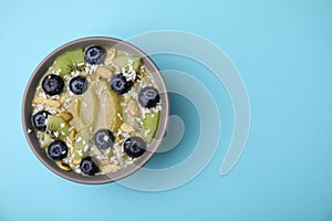 Bowl of delicious fruit smoothie with fresh blueberries, kiwi slices and coconut flakes on light blue background, top view. Space