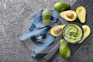 Bowl with delicious guacamole and ripe avocados on grey textured background